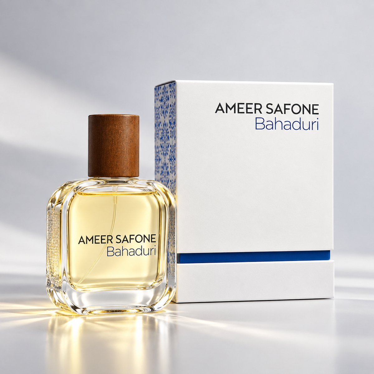 A bottle of Ameer Safone Bahaduri perfume with a brown cap stands next to its white box with blue accents on a light gray reflective surface.