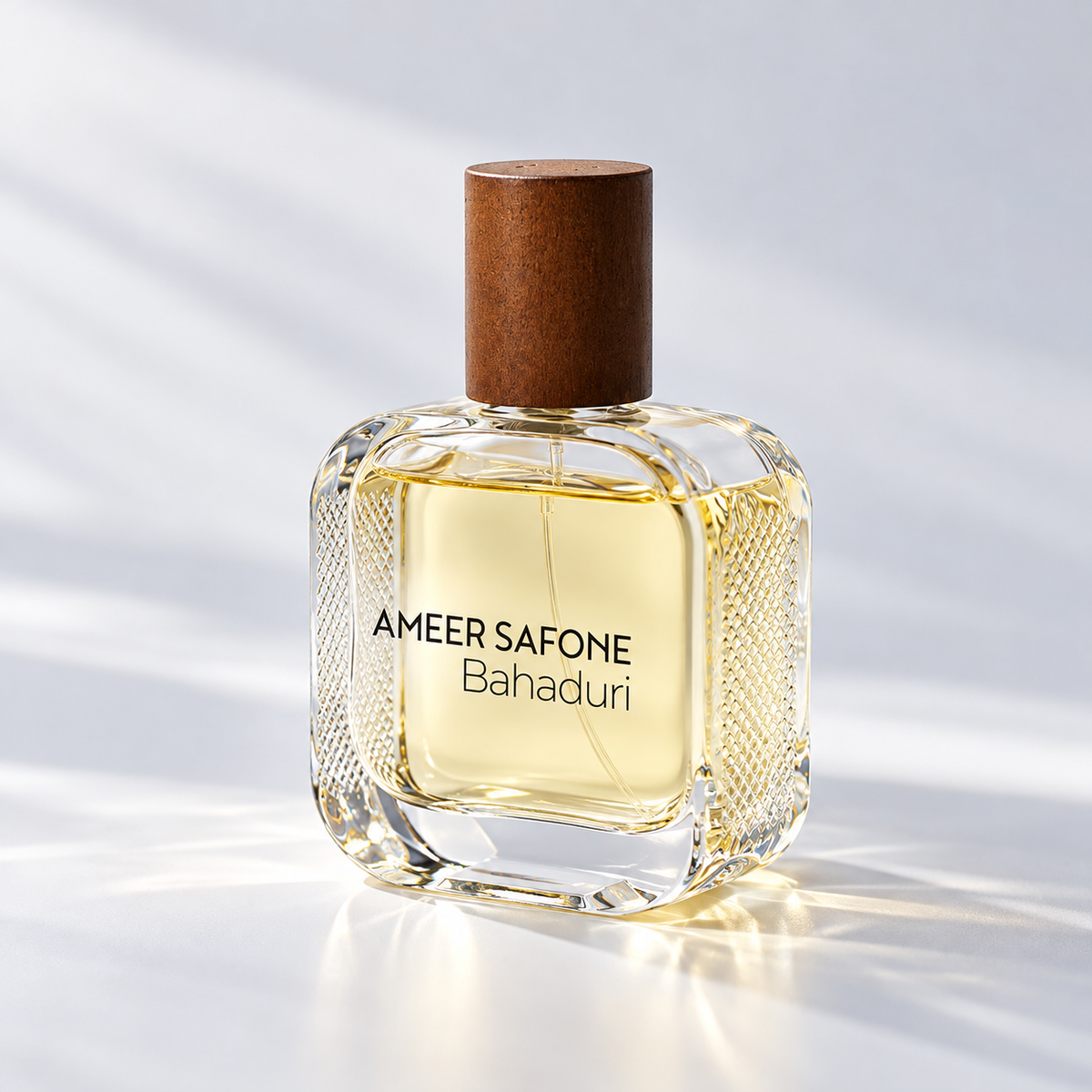 A bottle of Ameer Safone Bahaduri perfume with a textured clear glass body, light yellow liquid, and a brown wooden cap, set against a bright white background with soft diagonal shadows.